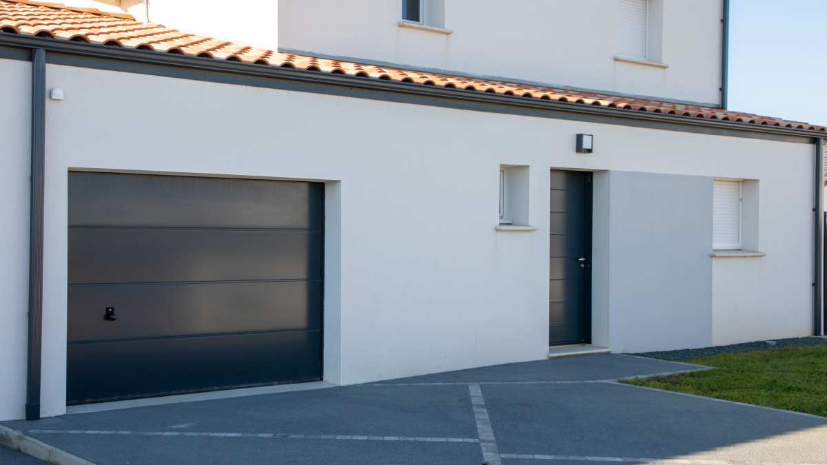 Zwarte aluminium garagedeur naast de voordeur van een woning.
